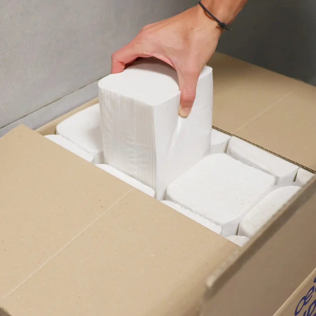 Karton mit Papierhandtüchern aus welchem ein Päckchen Handtücher rausgezogen wird